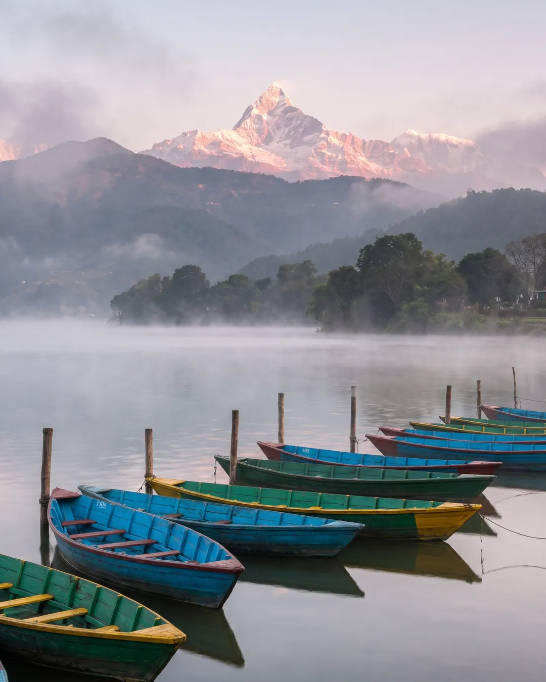 Phewa Lake at sunrise with boats on the shore and Machhapuchhre above the hills